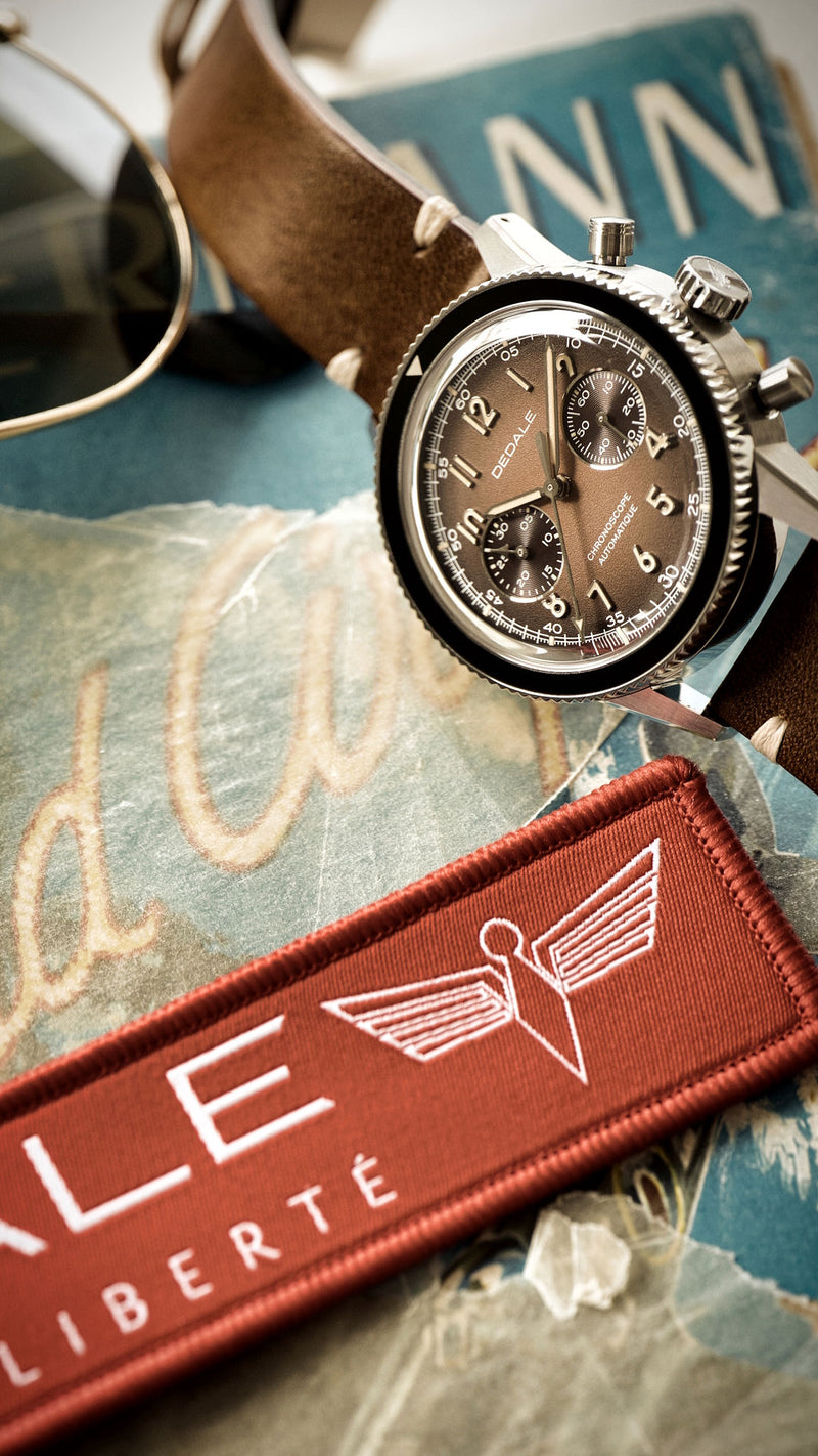 Montre d'aviateur DÉDALE WP-01 ALFA ZULU posée sur la première édition du livre 
