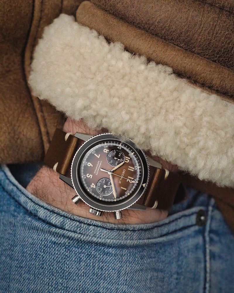 Chronographe d'aviateur DÉDALE Waypoint WP-01 ALFA ZULU avec son bracelet en cuir italien marron vintage porté par un pilote vétu d'un manteau bombardier en cuir de veau retourné.