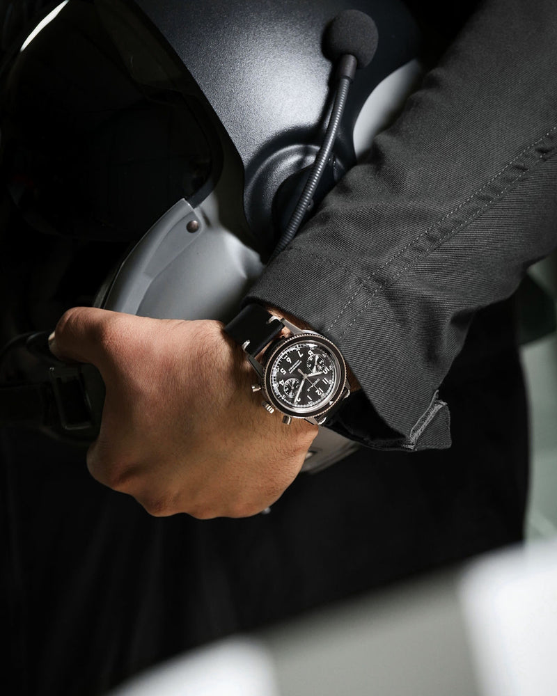 Chronographe automatique DÉDALE Waypoint WP-01 NOVEMBER au poignet d'un aviateur en combinaison de vol, casque de voltige à la main.